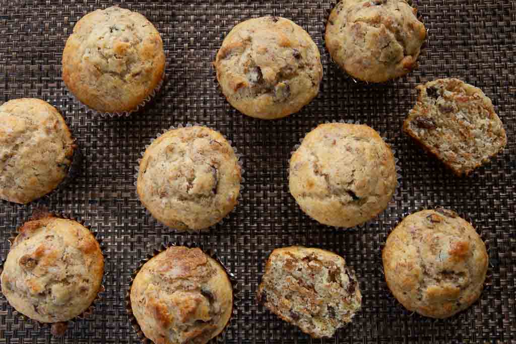 Eleven freshly baked raisin bran muffins on a brown mat.