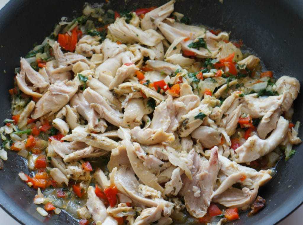 Chicken slices, herbs, diced onions, and peppers frying in a pan.