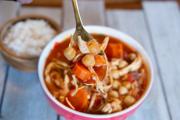 Bowl of chicken garbanzo bean soup with dish of white rice in the background.