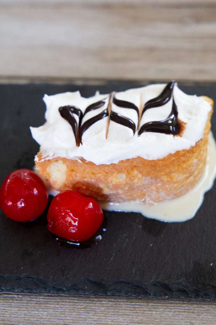 Slice of tres leches cake on a black slate board.