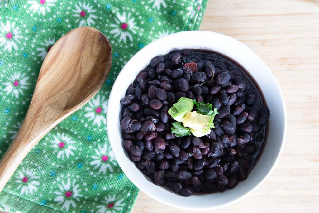 Bowl of black beans with avocado and cilantro garnish.