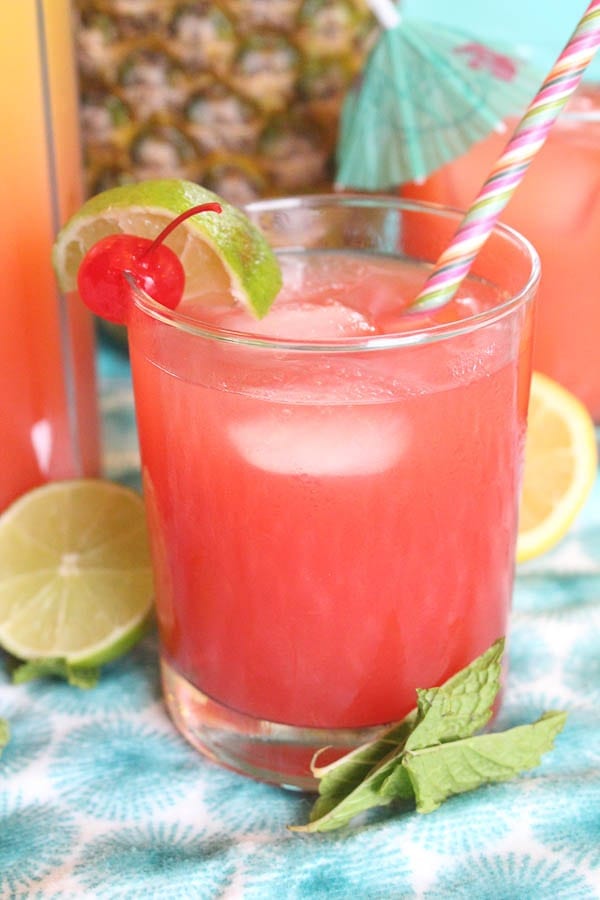 rum punch in glass with ice, cherry and lime garnish