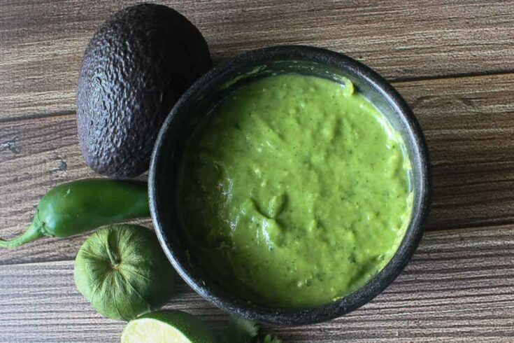 Bowl of green salsa accompanied by avocado and peppers.