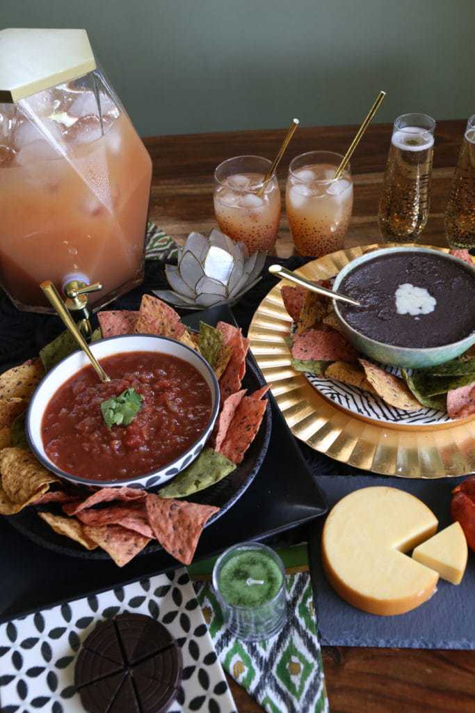 bean dip on table with guava cocktail, red salsa and cheese wheel