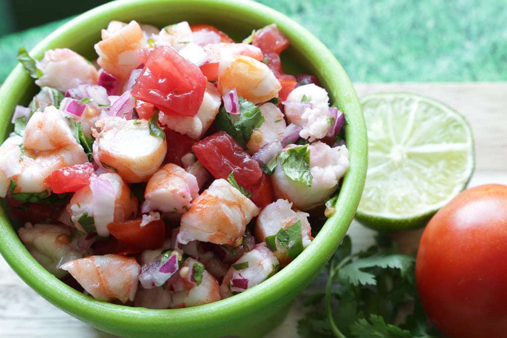 lime and tomato on cutting bowl with bowl of ceviche