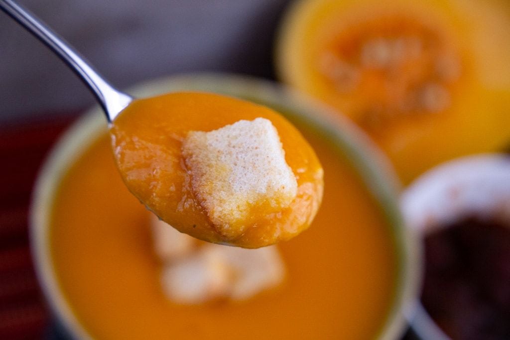 Silver spoon filled with butternut squash soup and a crouton.
