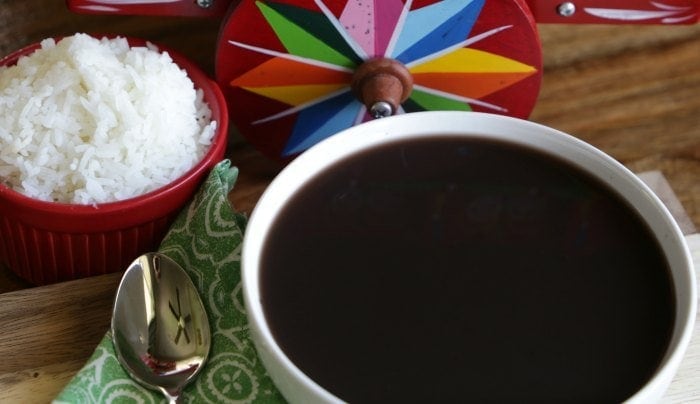 Black bean soup in a ceramic bowl beside a cloth napkin and spoon.