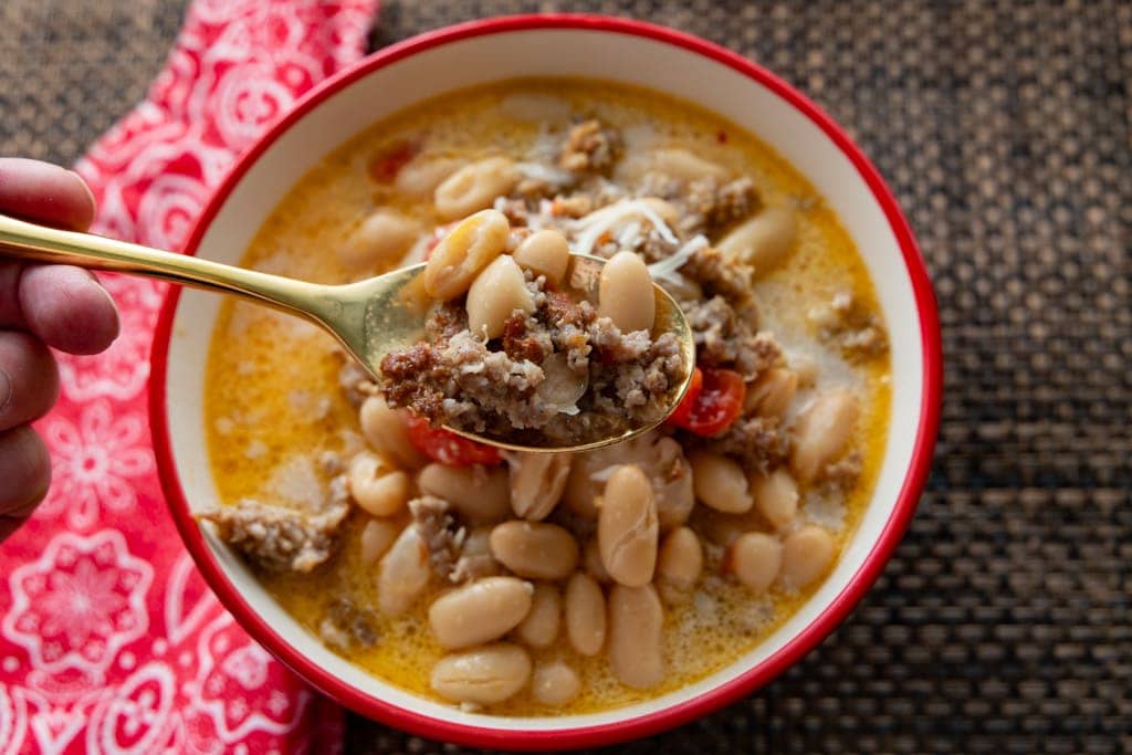 The spoon lifting up some of the sausage soup.
