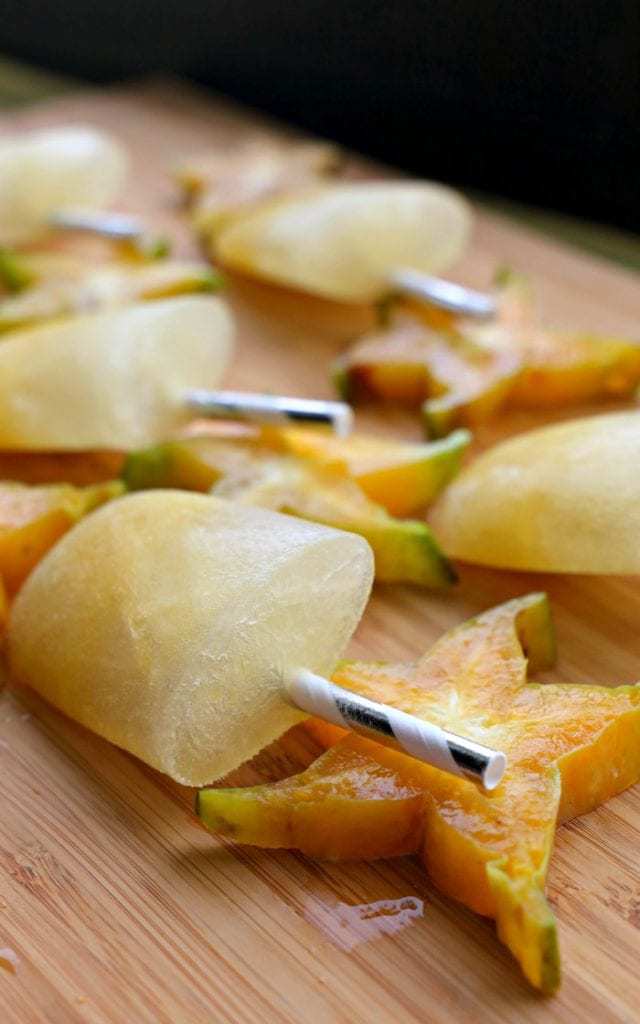 Frozen starfruit popsicles and starfruit halves arranged on a wooden cutting board.