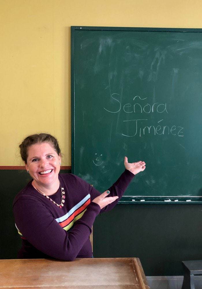 Spanish teacher in classroom in front of blackboard.