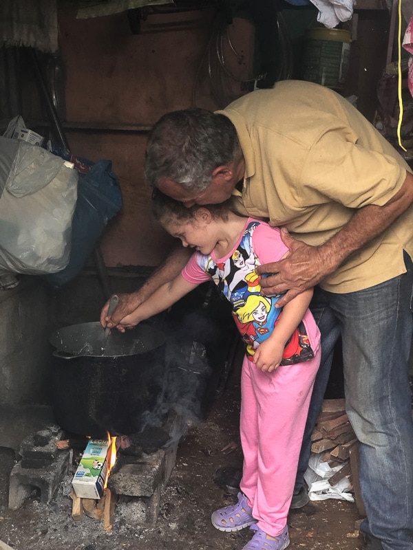 young girl stirring por of tamale masa over an open fire in costa rica with her uncle helping her
