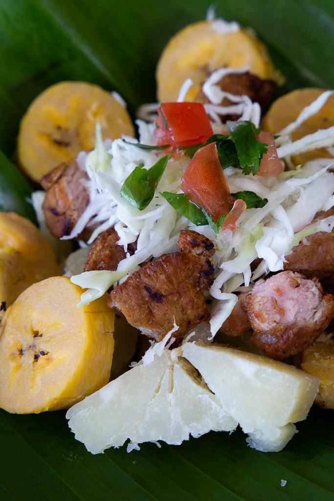 costa rican salad on a banana leaf with chicharron, lime, cabbage, chimichurri, yuca and green plantain