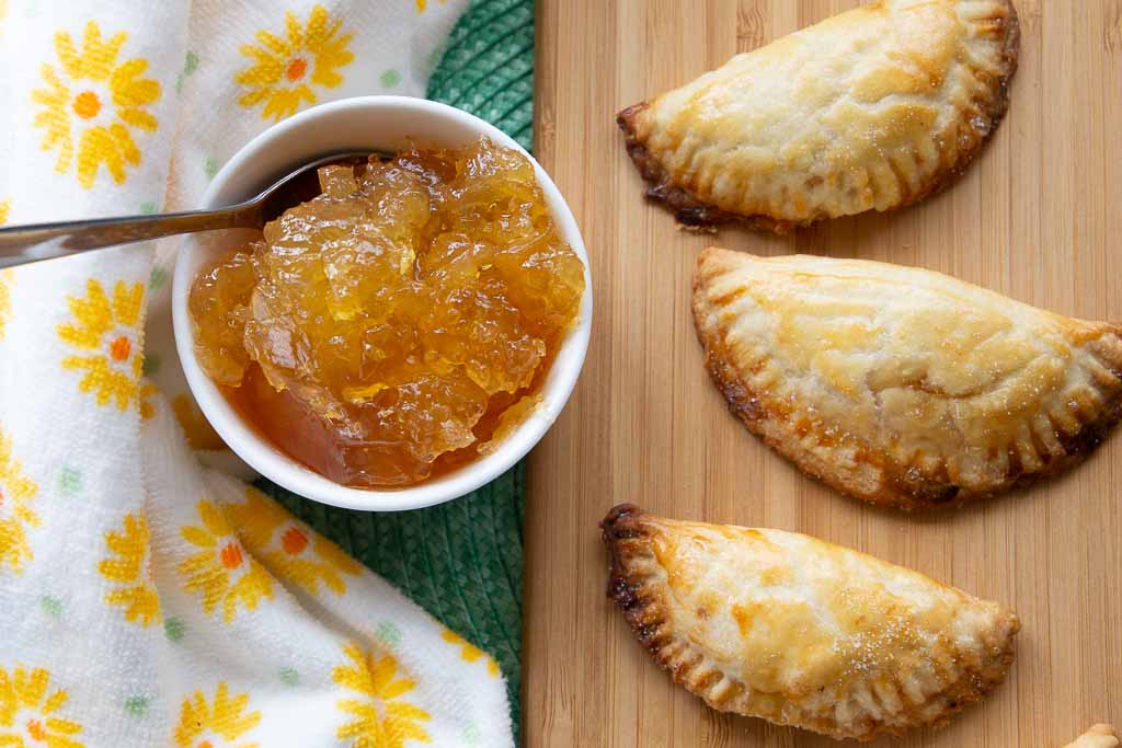 Three pineapple empanadas and a white ceramic dish of pineapple preserves.