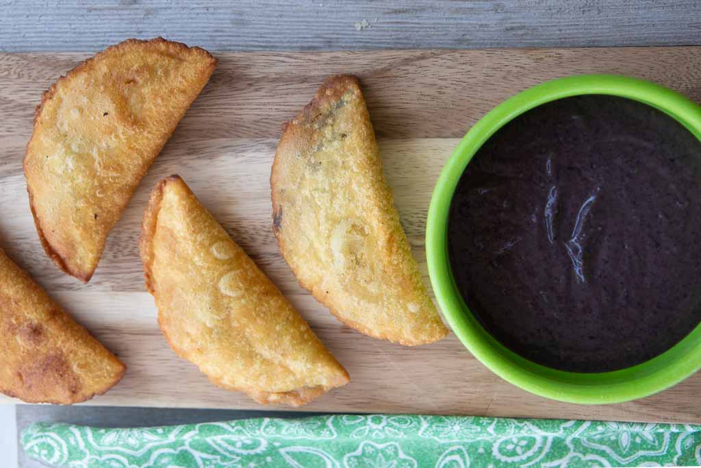 Four bean empanadas and green bowl of black bean puree.