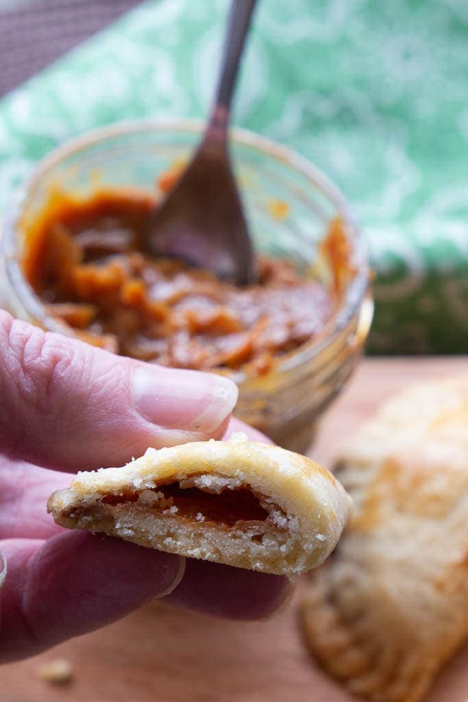 Fingers holding a dulce de leche empanada morsel.