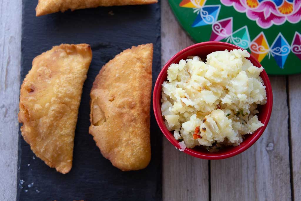 Vegan potato empanadas and small red rampkin of filling.