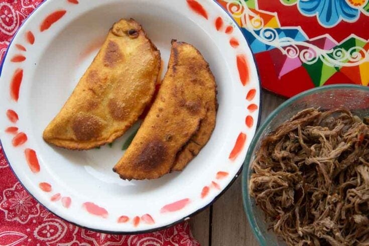 Two beef empanadas accompanied by a bowl of shredded beef.