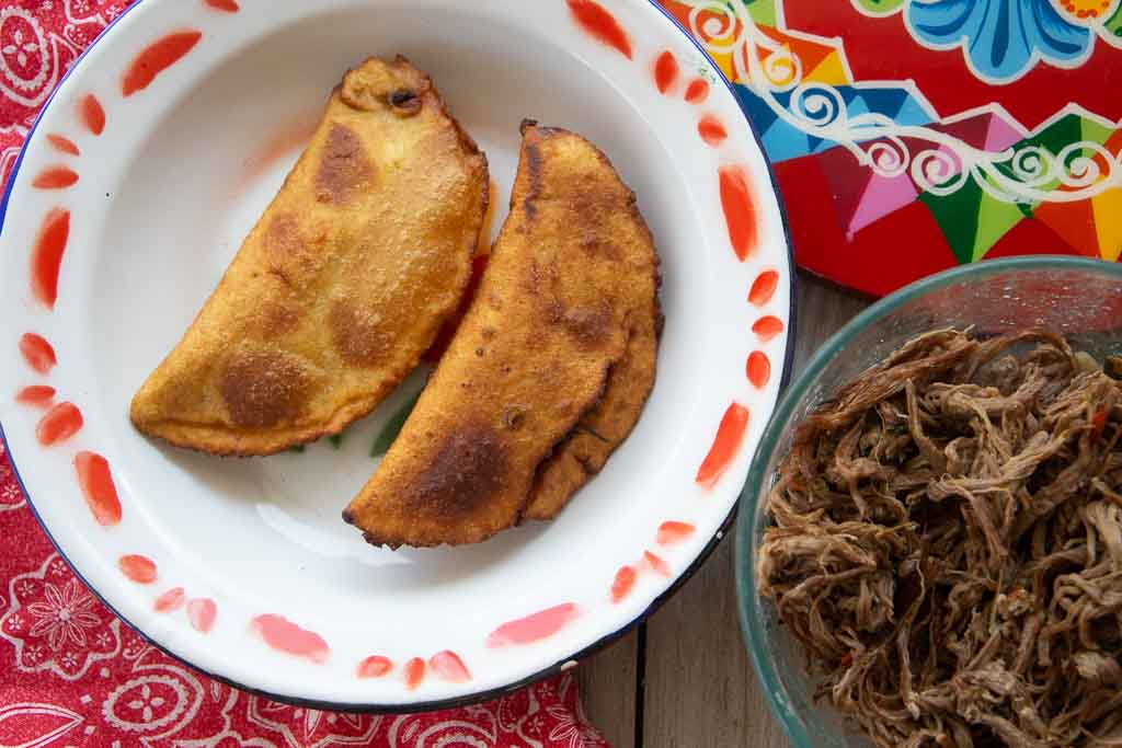 Two beef empanadas accompanied by a bowl of shredded beef.