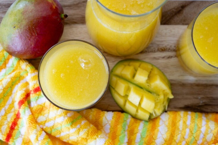 Aerial view of several glasses of mango juice and mango fruits.