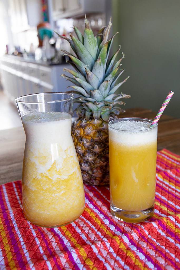 Fresh pineapple juice with a purple striped straw resting on a multicolored cloth.