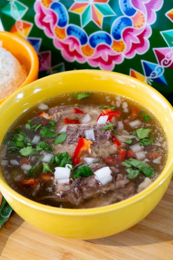 Yellow bowl of beef soup with a traditionally painted disc in the background.