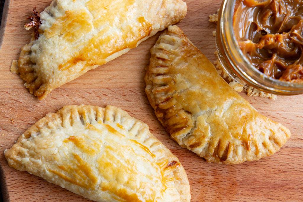 Close up of three freshly baked empanadas beside a jar of cajeta.