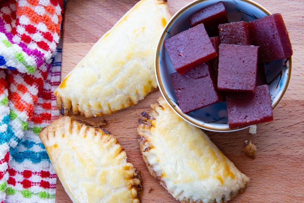 Bowl of guava paste wedges beside three freshly baked empanadas.