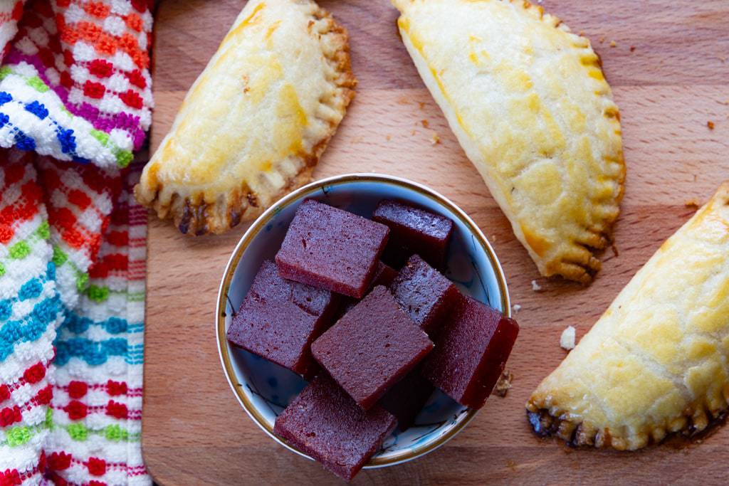 Three baked empanadas arranged around a small blue bowl of guava paste.