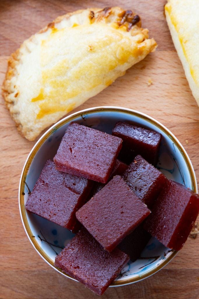Bowl of guava paste squares beside a single baked empanada.