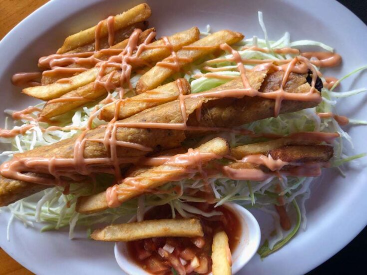 Costa Rican style taco on a bed of cabbage and drizzled with pink sauce.