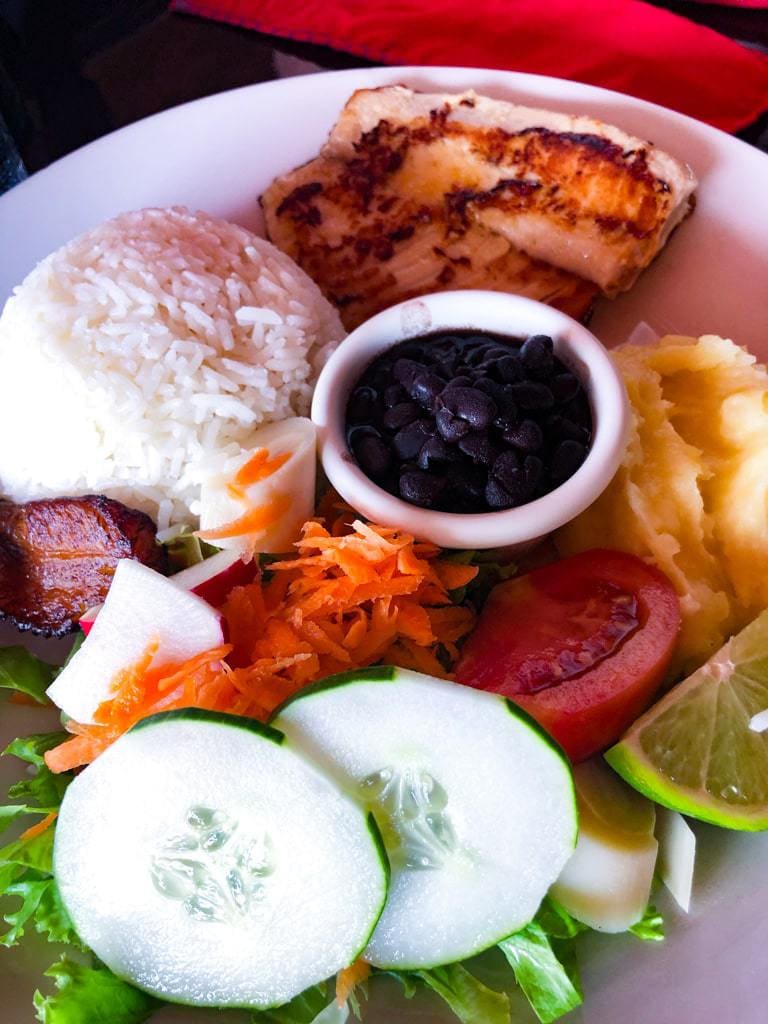 White platter with portions of rice, salad, black beans, and meat.