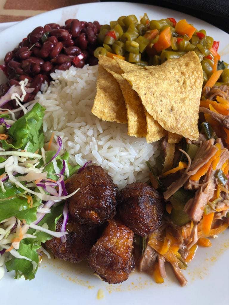 Mound of white rice ringed by fried plantains, beans, meat, picadillo, and salad on a white platter.