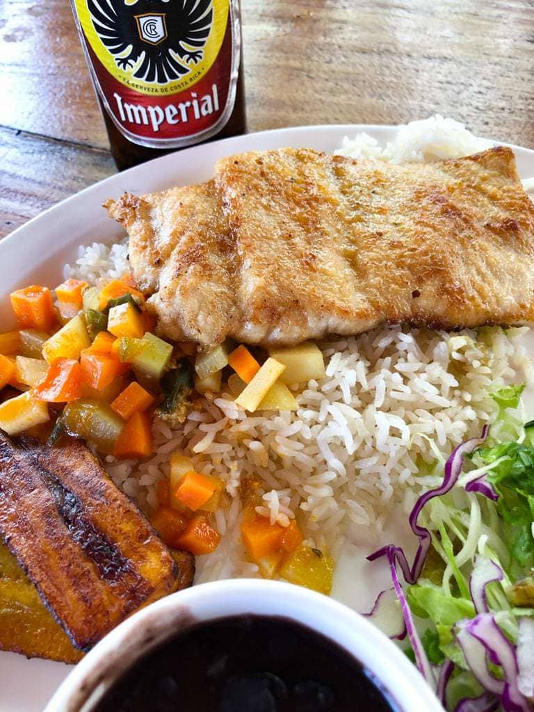 Costa Rican casado platter with servings of picadillo, beans, white rice, and salad beside a can of Imperial beer.