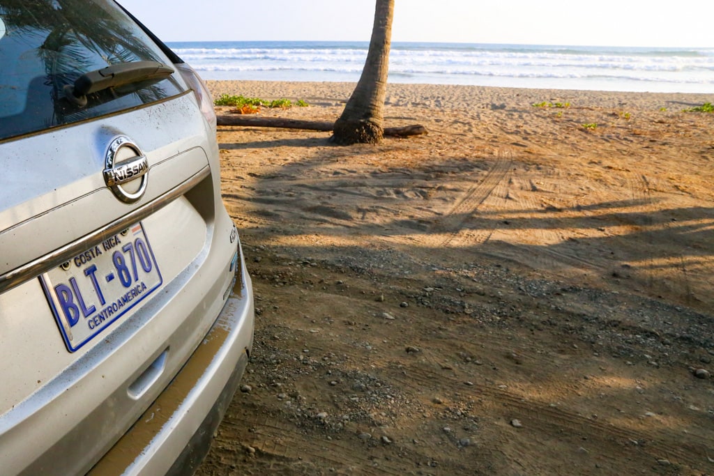 costa rician beach next to rental car .