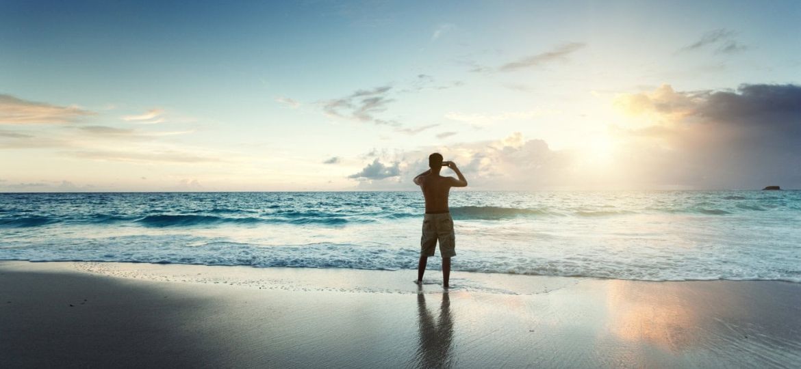 Young,Man,On,The,Beach,Take,Photo,On,Mobile,Phone